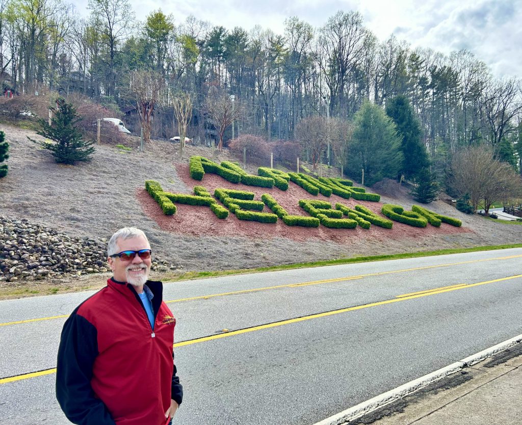 Curtis is standing in front of a topiary that welcomes travelers to Helen, Georgia.