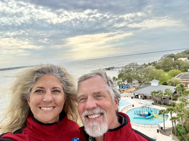 Laura and Curtis enjoy the view of the Brunswick River estuary and the Atlantic Ocean from the St. Simons Lighthouse balcony. Neptune Park and the pier can also be seen below.